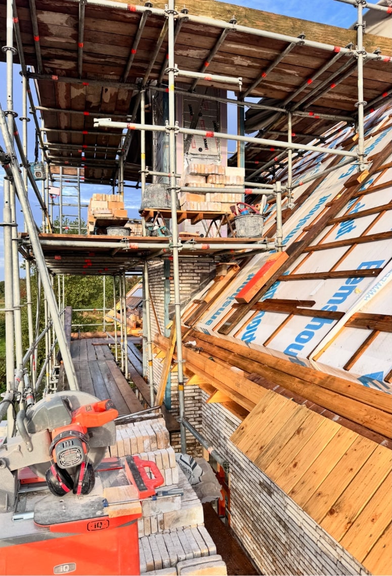 Steiger op het dak van een nieuwbouwwoning in Castricum, met de steenzaag en de stenen voor de schoorsteen