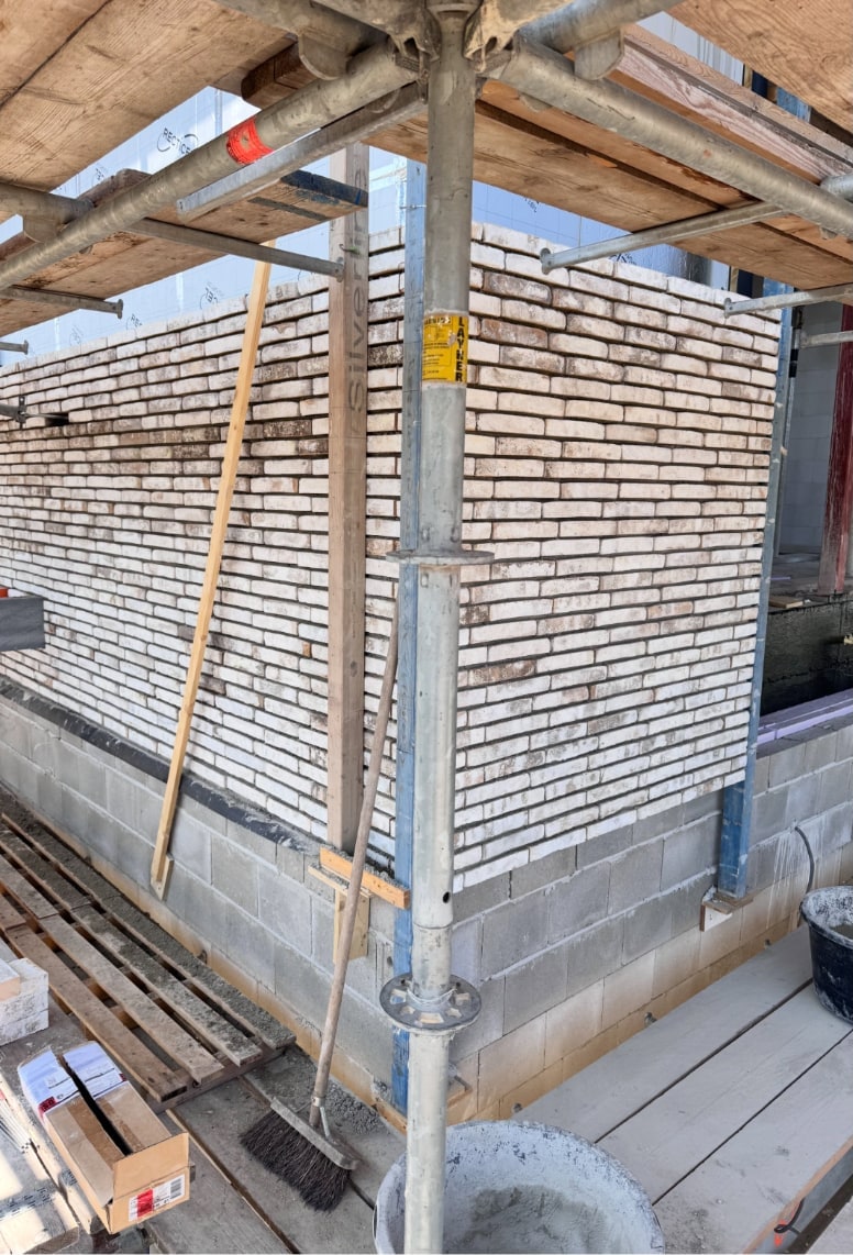 Hoek van een vers gemetselde witgrijze muur op een betonnen plint, in de steiger