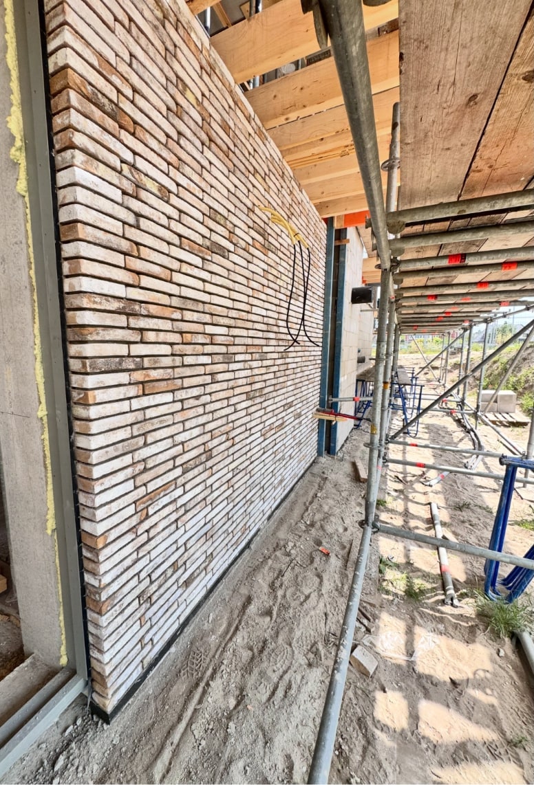 Lange witgrijze gemetselde muur in de steiger, de kabels voor de buitenlamp steken nog uit