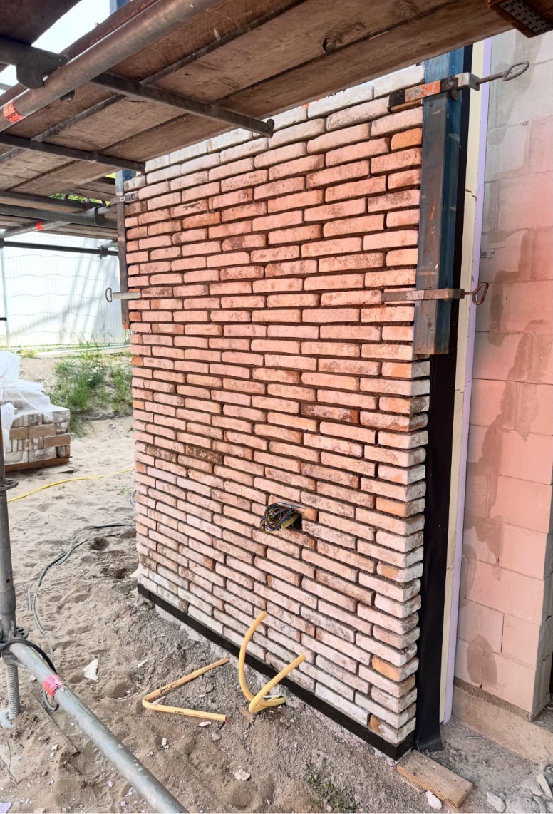 Vers gemetselde oranjerode muur naast een bestaande wand, de specie nog nat