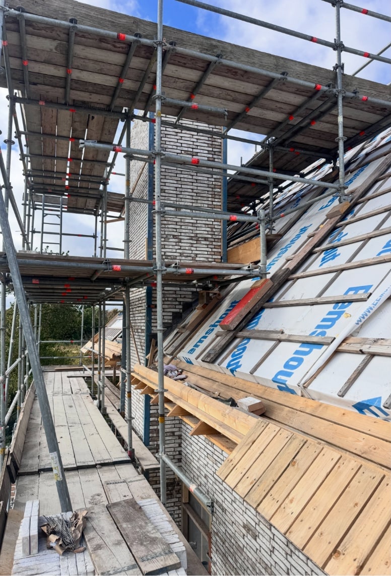Gemetselde schoorsteen van witgrijze steen op een nieuwbouwdak, nog in de steiger